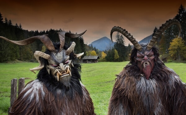 Two Krampus figures with fur and horns in the mountains